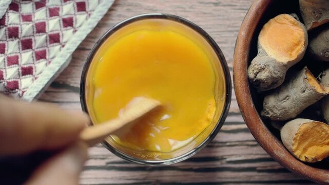 Combining turmeric powder with water inside a glass container
