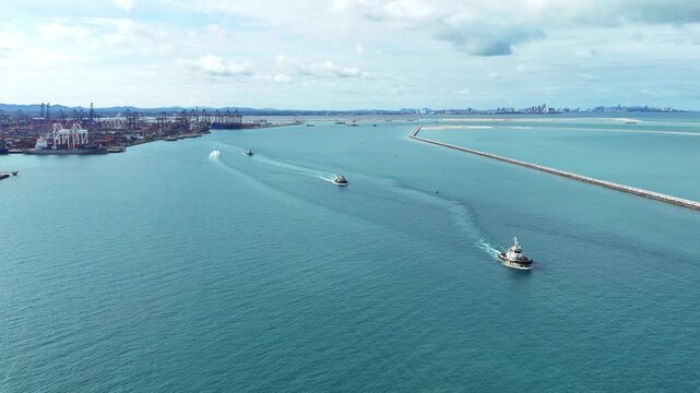 tugboats sailing through clear blue sea water near a concrete breakwater. Maritime logistics support, harbor navigation, and commercial port operations concept.