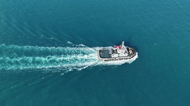 tugboats sailing through clear blue sea water near a concrete breakwater. Maritime logistics support, harbor navigation, and commercial port operations concept.