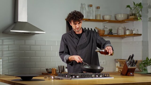 Male cook pours alcohol into a frying pan, creating a dramatic burst of flames during a slow motion flamb&eacute; in a home kitchen.