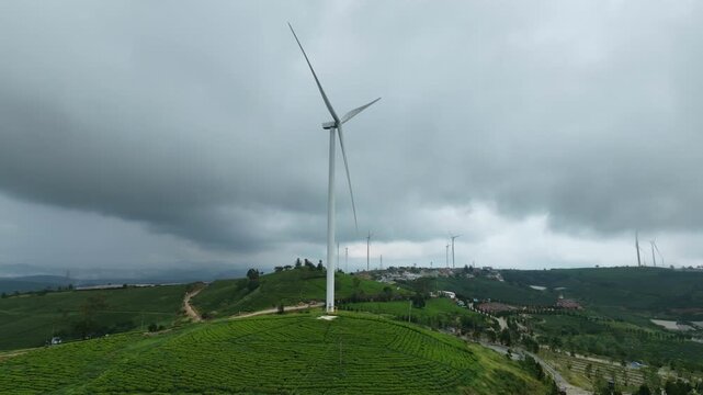 Aerial static view of wind turbine spinning on green Cau Dat Tea Hill under cloudy sky,  Da Lat, Vietnam