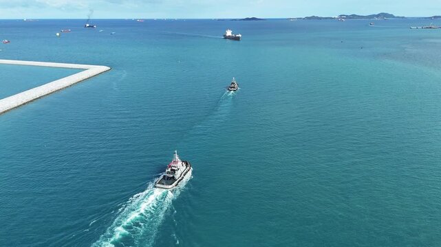 tugboats sailing through clear blue sea water near a concrete breakwater. Maritime logistics support, harbor navigation, and commercial port operations concept.