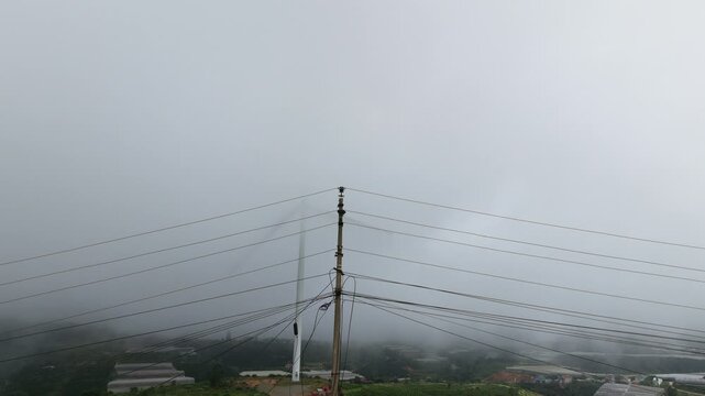 Static shot of fog enveloping power lines and rooftops in misty hillside setting Cau Dat, Da Lat, Vietnam 