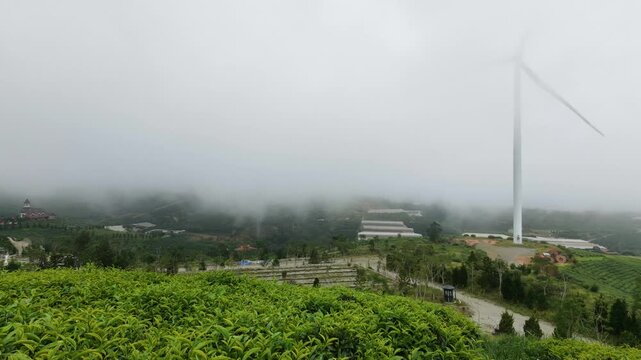 Static shot of wind turbine rotating in foggy mountain landscape with greenery  Tea Hill Cau Dat, Da Lat, Vietnam 