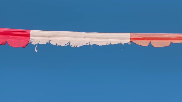 Red and white hazard warning tape fluttering against a clear blue sky, construction zone security, danger restriction