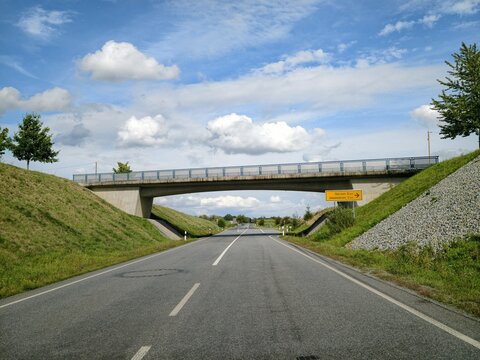 Empty country road under concrete overpass with blue sky, clouds, and guardrails