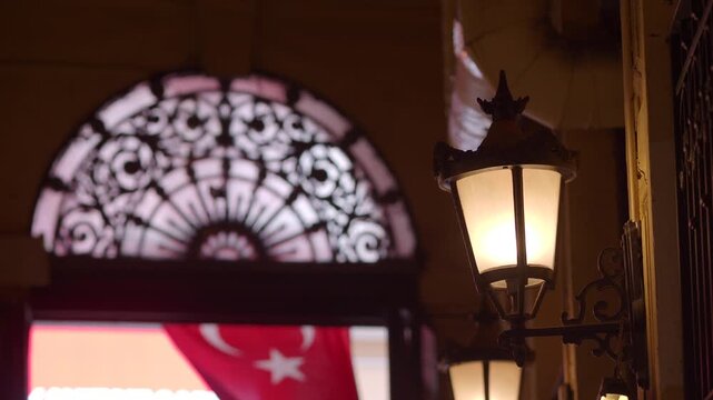 Ornate vintage street lamp glows at night near arched doorway with Turkish flag.