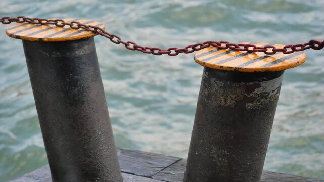 Industrial metal bollards with yellow stripes on pier against rippling river water motion.