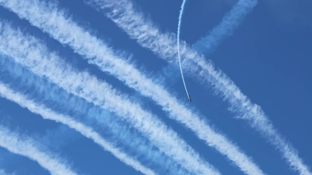 Airshow acrobatics with planes creating thick white smoke trails in clear blue sky.