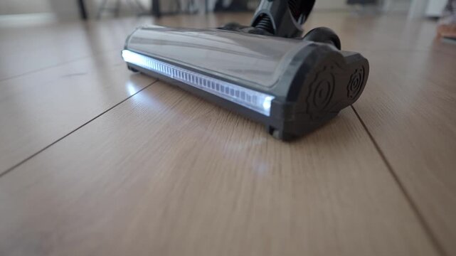 Close up slow motion footage of vacuum cleaner head moving across wooden floor.