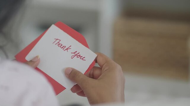 Close-up of woman's hands removing a thank you card from a red envelope.
