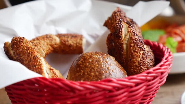 Close up of fresh bread rolls and bagels in red basket with white paper liner.