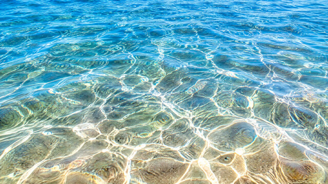 Clear blue water surface with sunlight caustic patterns and ripples in a shallow tropical sea