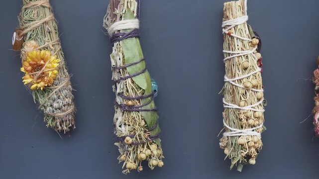 Close up of dried herbs and flowers bundled together hanging on dark background.