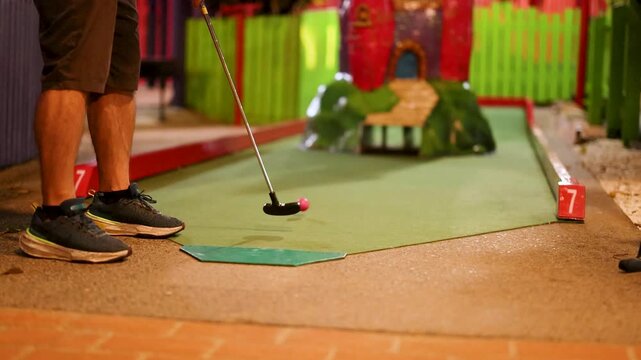 Person playing mini golf on colorful course with castle obstacle during daylight.