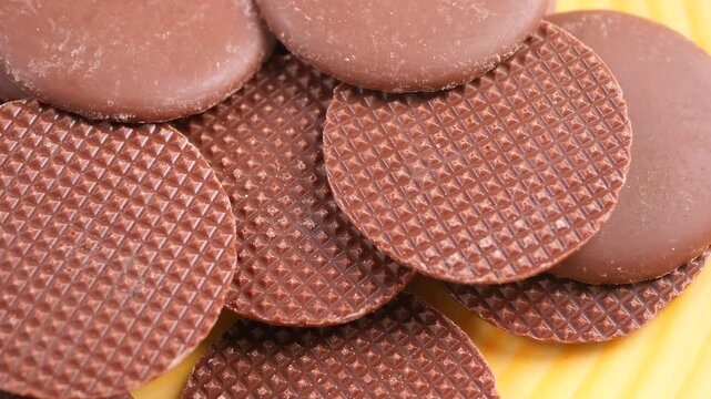 Milk chocolate rounds with textured pattern rotating on yellow surface in macro slow motion.