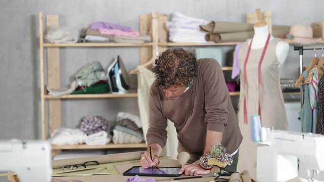 Using artificial intelligence in clothing production. Man seamstress draws image of future suit on tablet, creates electronic prototype of finished product. 