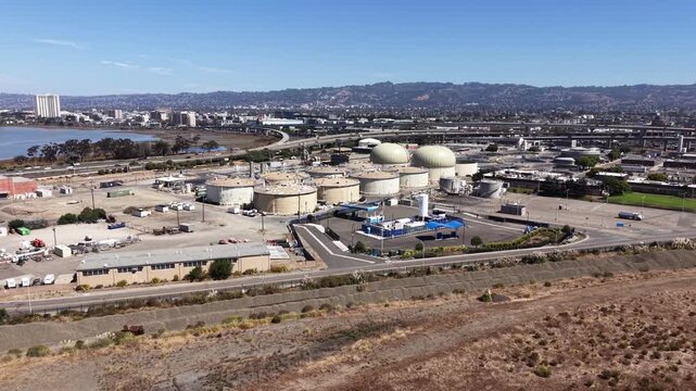 Sideways aerial shot of the East Bay Municipal Utility District wastewater treatment plant in Oakland, California, showing storage tanks and facilities with the city skyline in the background