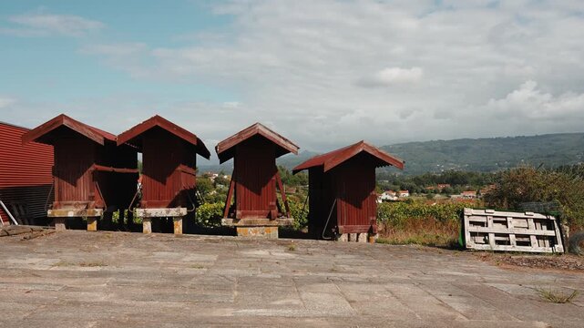 Row of wooden espigueiros raised on stone pillars stands on a threshing floor above the hills of northern Portugal.