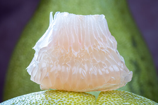 A single juicy pomelo fruit segment presented on a small ceramic stand with pomelo rind background.