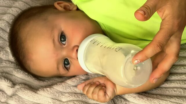 Baby drinks milk from a bottle while lying on a bed at home, infant feeding, childhood nutrition, peaceful care routine and early development.