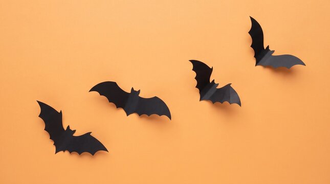 Silhouette of several bats in flight against a warm orange sunset or sunrise sky creating a dramatic scene