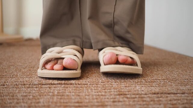 Person wearing light brown criss cross strap slides on woven rug footage.