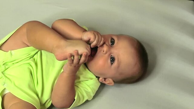 Infant holds a foot and puts toes in the mouth while lying at home, sensory exploration, motor development, curiosity and early childhood discovery.