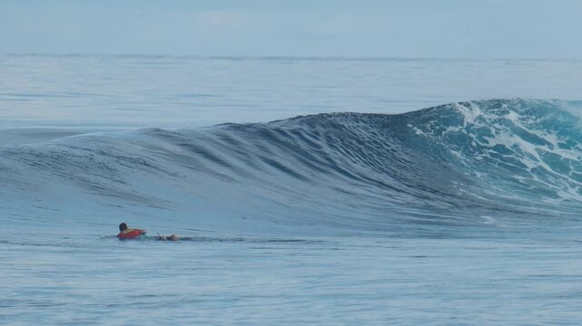 Surfer paddles towards the line up on the uncrowded surfing spot of the Sultans in the Maldives with the big and perfect glassy waves