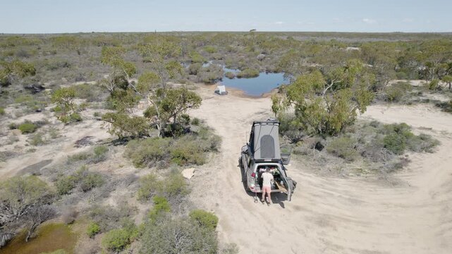 Man Cooking At Rear Of 4WD On Dirt Track In Dry Australian Outback