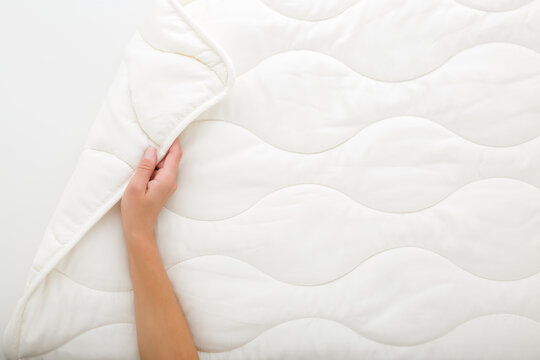 Young adult woman hand holding new clean white soft fibre duvet on light gray background. Closeup. Flat lay. Top down view.