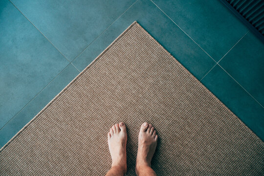 Bare feet standing on a textured carpet beside a tiled floor. Home comfort, minimalist interior and residential flooring concept.