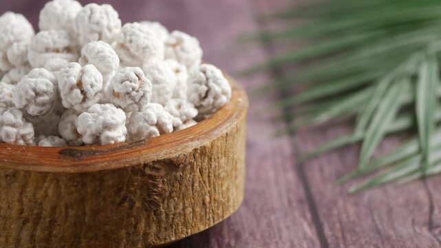 Roasted chickpeas with sugar coating in wooden bowl rotating slowly on dark wood background.