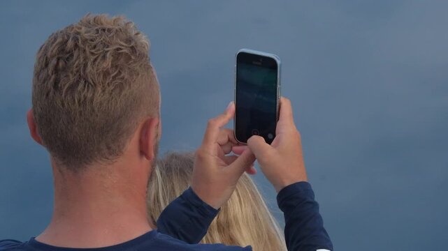 Person sits on the boat moving in the calm sea and takes a photo with smartphone