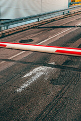 Lowered red and white boom gate barrier across a sloped asphalt road ramp with a painted white arrow. © Bits and Splits