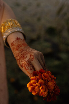 Close-up of a woman's hand decorated with intricate henna mehndi patterns and golden traditional bangles, holding vibrant orange marigold flowers during Diwali festival celebration.