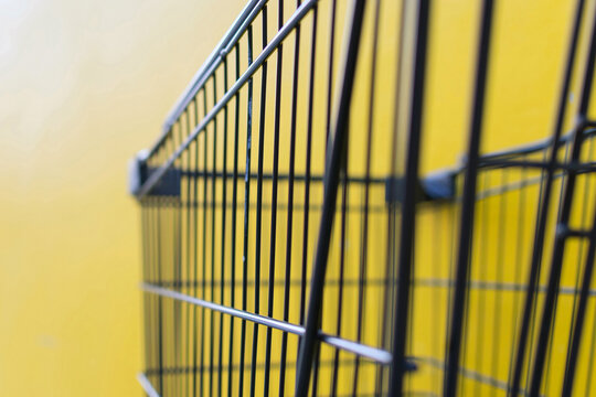 Close view of an empty black wire shopping basket against vivid yellow background copy space for retail consumer spending commerce themes