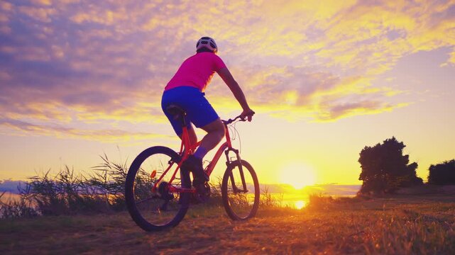 A senior adult enjoys a ride on an orange mountain bike against a vibrant sunset, blending cycling with an active lifestyle in a serene natural setting.