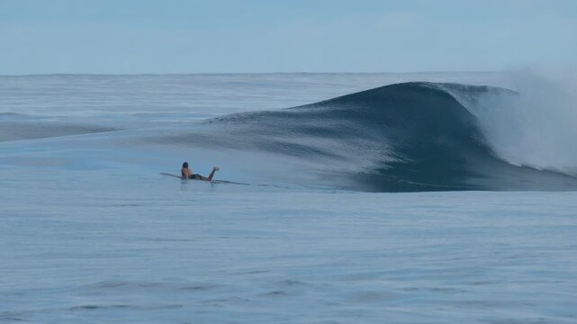 Surfer paddles towards the line up on the uncrowded surfing spot of the Sultans in the Maldives with the big and perfect glassy waves