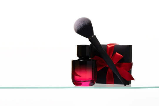 Elegant makeup brush, red gradient perfume bottle, and black gift box with a red satin bow on a glass surface. Perfect for luxury beauty sales, cosmetics gifting, and holiday fragrance promotions.