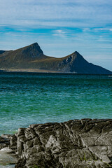 Vertical view of a rocky coastline with turquoise sea water and majestic mountain peaks under a blue cloudy sky in Norway © Quality by Simon