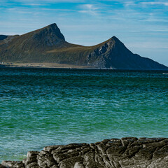 Vertical view of a rocky coastline with turquoise sea water and majestic mountain peaks under a blue cloudy sky in Norway © Quality by Simon
