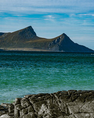 Vertical view of a rocky coastline with turquoise sea water and majestic mountain peaks under a blue cloudy sky in Norway © Quality by Simon