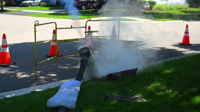 Steam Cured CIPP Trenchless Sewer pipe rehabilitation process with vapor rising from underground pipeline equipment on a residential street