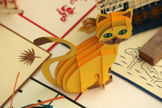 Handmade 3D popup paper greeting card in the shape of a yellow cat sitting among other papercraft designs in Hoi An, Vietnam.