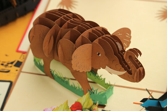 Detailed 3D popup paper card shaped like a brown elephant standing on a green grass cutout in Hoi An, Vietnam.