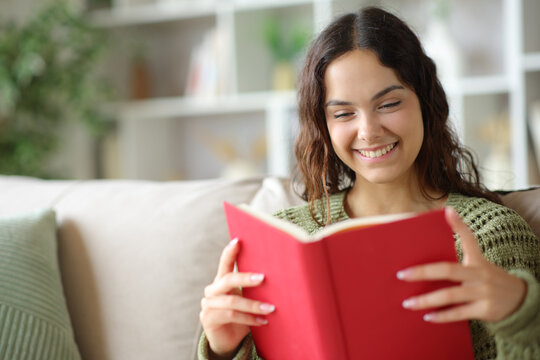 Happy young woman reading a red paper book at home