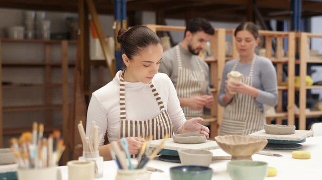 In pottery workshop, girl sitting at table, busy making products from raw clay. Amateur busy at master class modeling clay plates from clay 