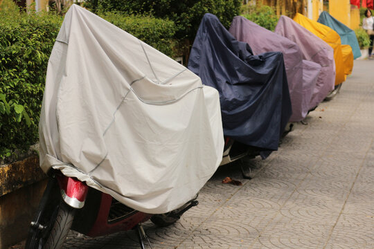 Row of motorbikes parked on a city street covered with colorful waterproof protective tarps to protect against rain and dust in Hoi An, Vietnam.