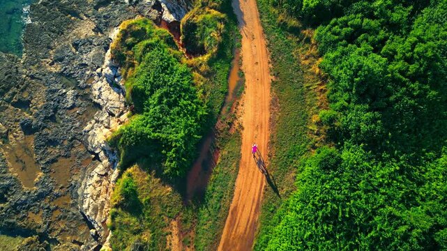 A senior cycles along a coastal dirt path surrounded by lush greenery and rugged cliffs, embracing an active lifestyle. The scenic route offers a perfect blend of nature and adventure.